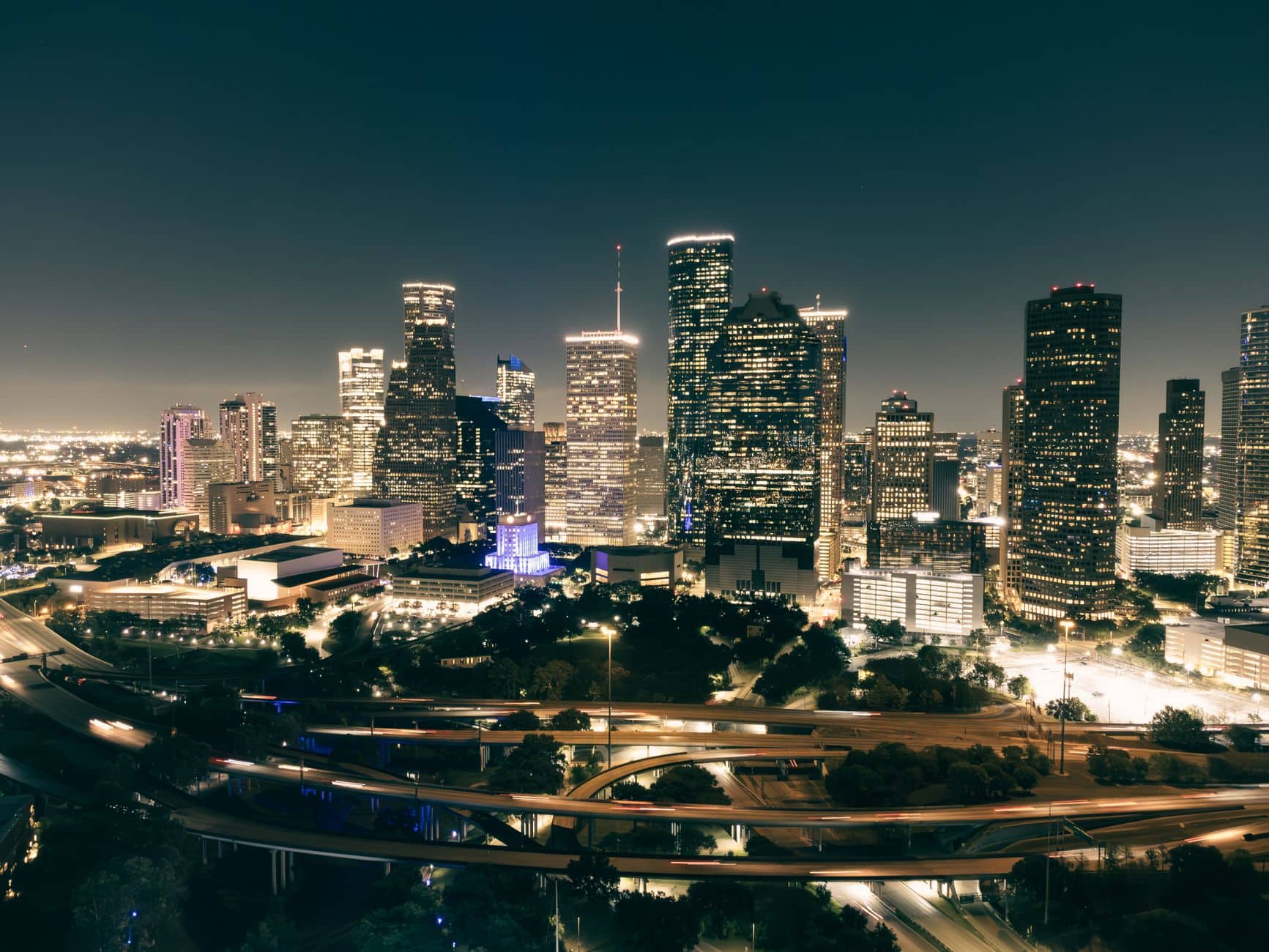 The downtown Houston skyline at night above the freeway interchange — the scale of the commercial market.